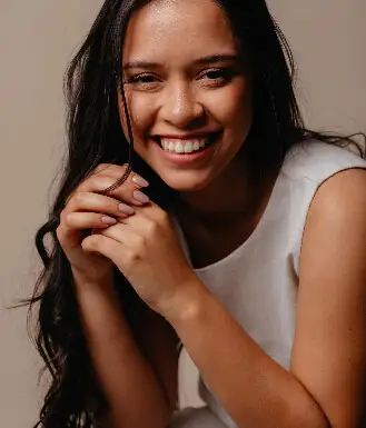 Larissa Oliveira sorrindo, de blusa branca, com as mãos junto ao rosto