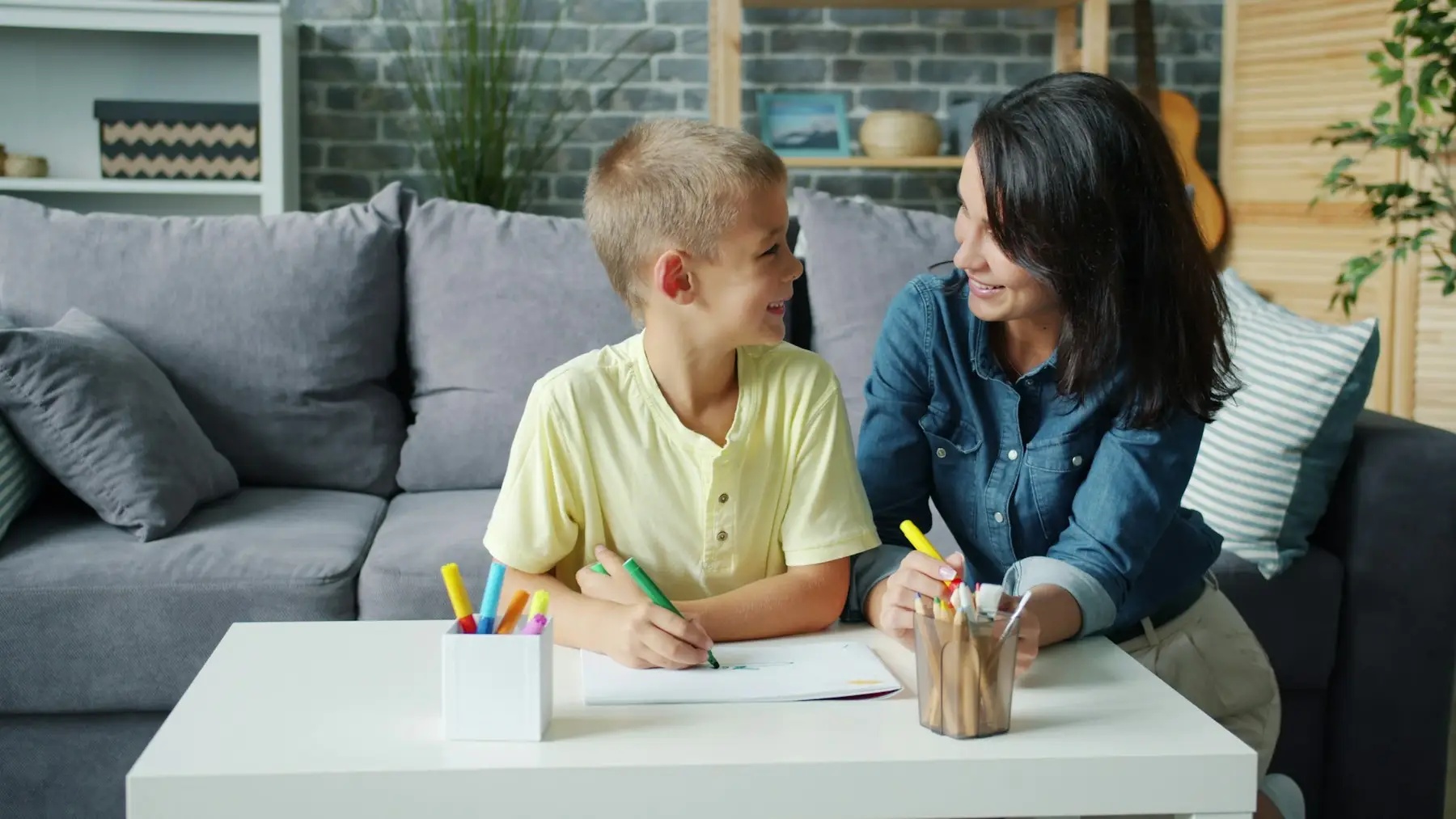 Mãe e filho desenhando juntos à mesa, com lápis de cor